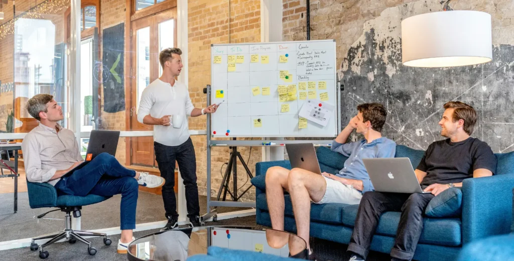 About Fourlogic. Team working with Compliance and Security Services sitting a couch looking at a whiteboard.